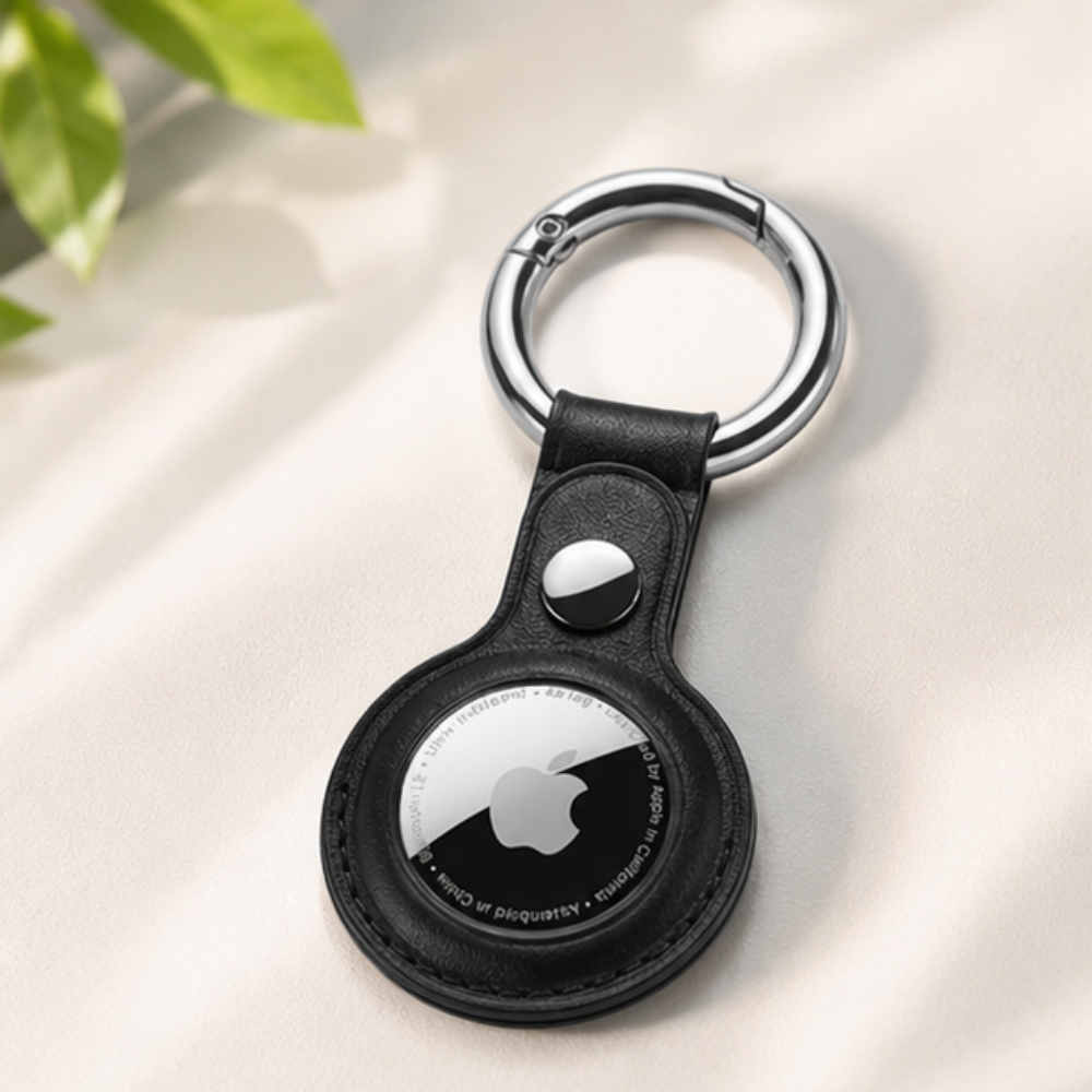 Apple AirTag in a sleek black leather key ring holder displayed on a light blue surface, showcasing the front-facing AirTag logo and keychain loop