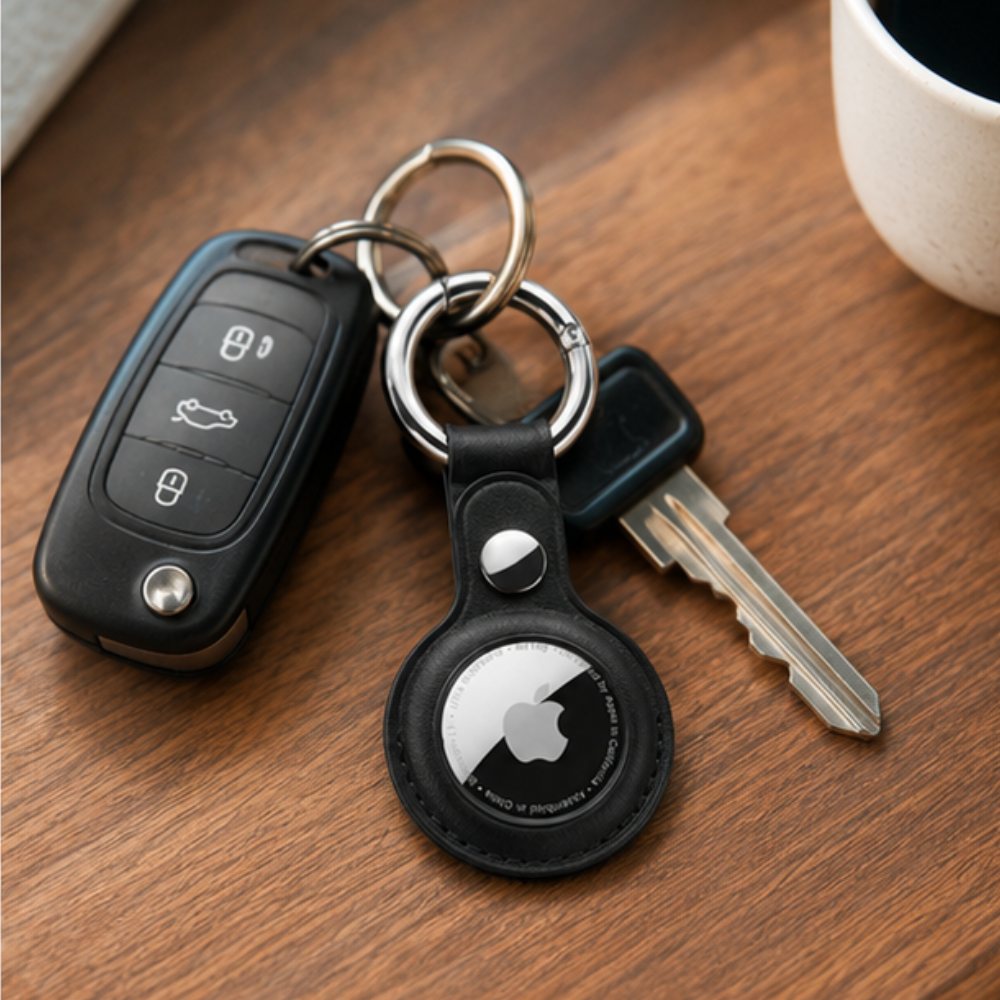 Apple AirTag in a black leather keychain holder attached to a set of car keys, placed on a wooden surface in a lifestyle setting