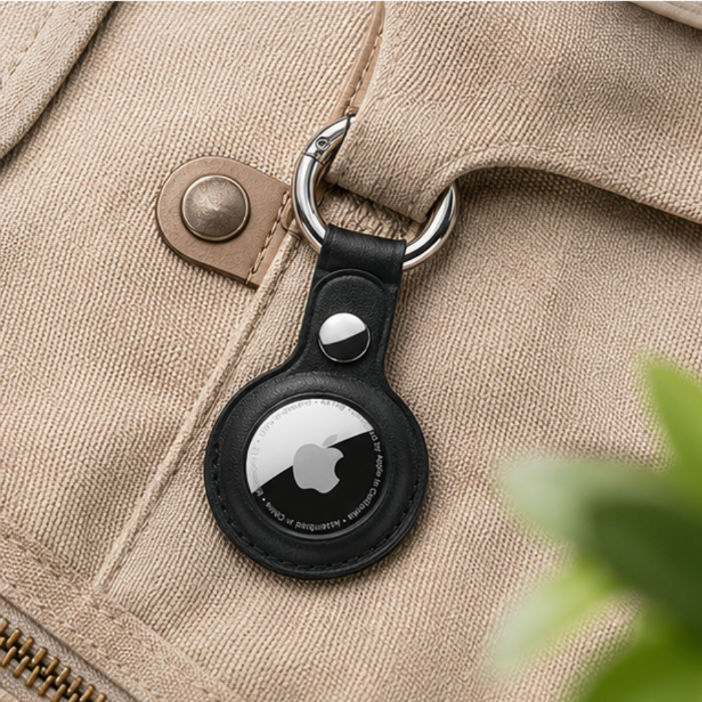 Apple AirTag in a black leather protective case with a metal keyring, clipped onto the zipper of a beige canvas bag