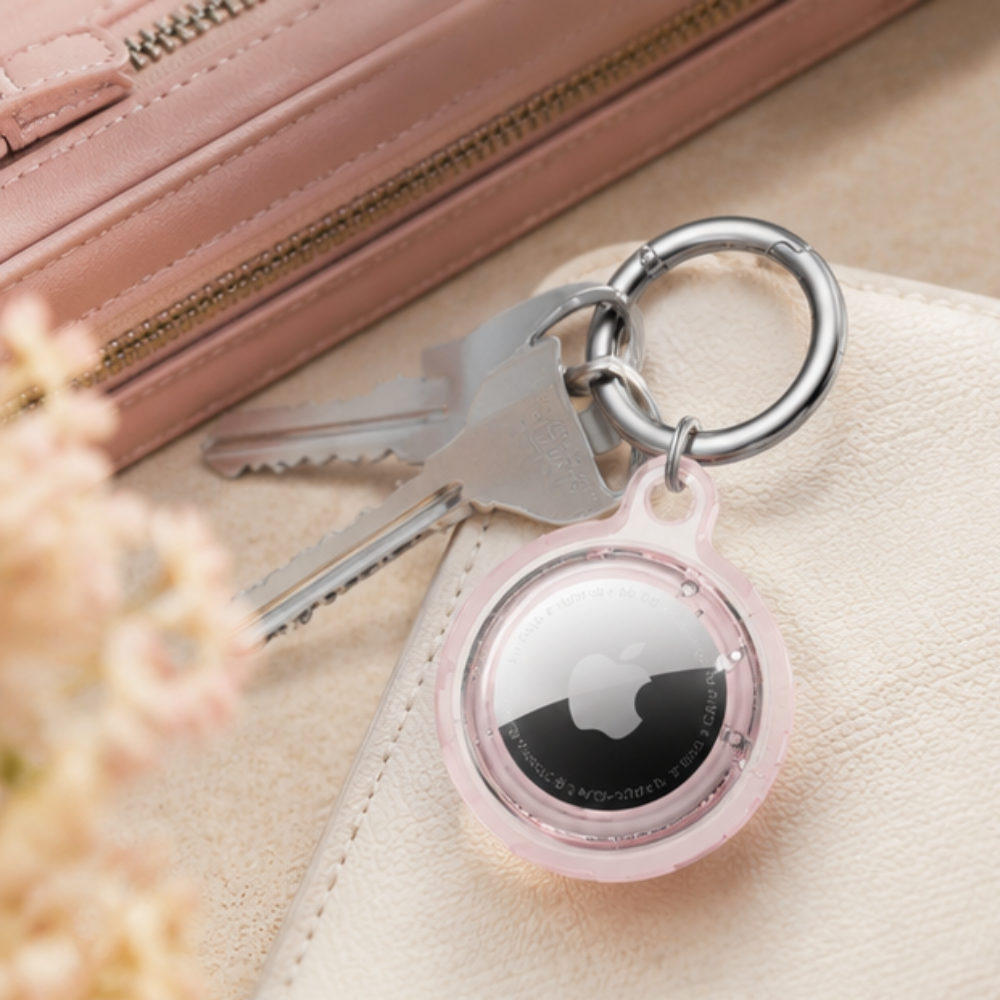 Apple AirTag in a light pink transparent keychain holder displayed on a pink surface, showcasing the clear case design and metal keyring loop