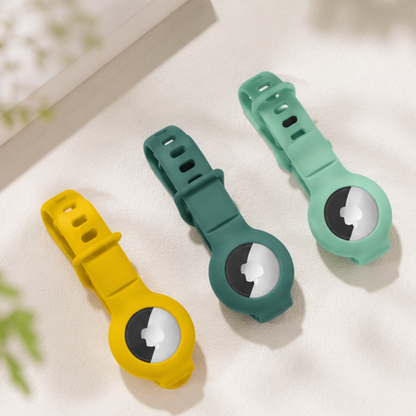 Three Apple AirTag silicone wristband holders in yellow and green colors displayed together on a light blue background, showing the adjustable strap and AirTag slot design