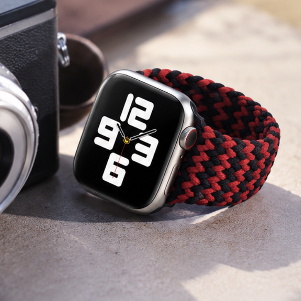 Person wearing Apple Watch with black and red braided solo loop band on their wrist, with headphones visible in the background