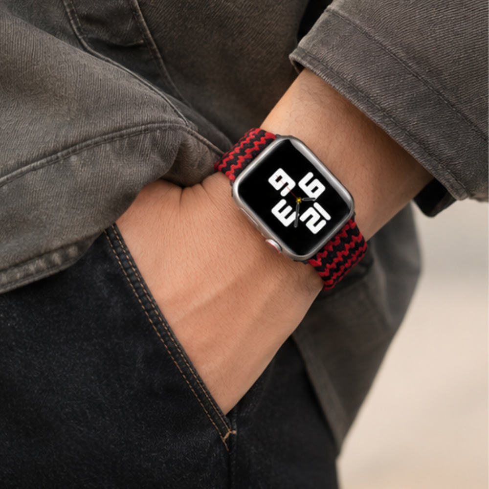 Close-up of a person in grey pants wearing Apple Watch with black and red braided solo loop band, showing the stretchable band detail