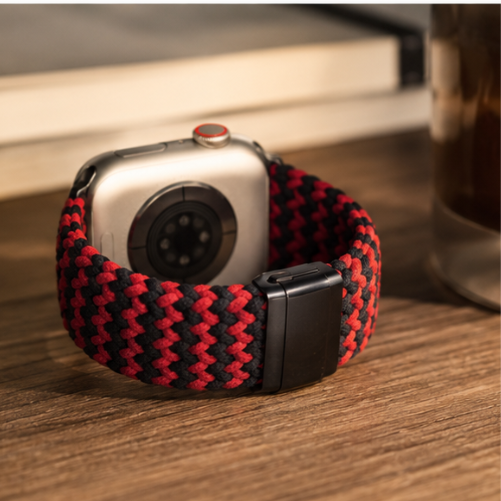 Rear view of Apple Watch with silver case and black and red braided solo loop band placed on a wooden surface, showing back sensors