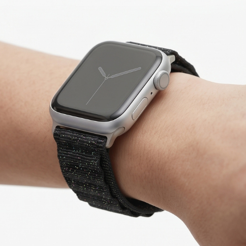 Person wearing an Apple Watch with a black nylon sport loop band on their wrist, shown from a close-up angle against a neutral background