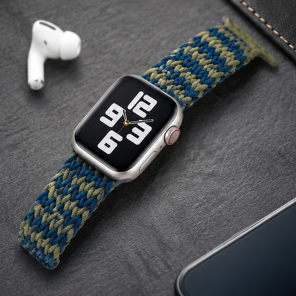 Close-up of an Apple Watch with a blue and green zigzag braided solo loop band worn on a wrist, highlighting the colorful woven texture of the band