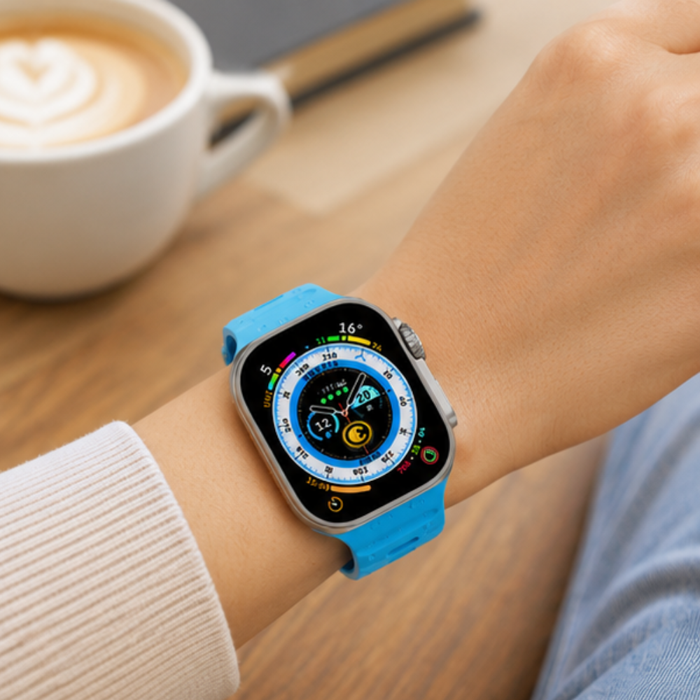 Person wearing an Apple Watch Ultra with a sky blue rubber sport band on their wrist, with a coffee cup visible in the background in a casual lifestyle shot