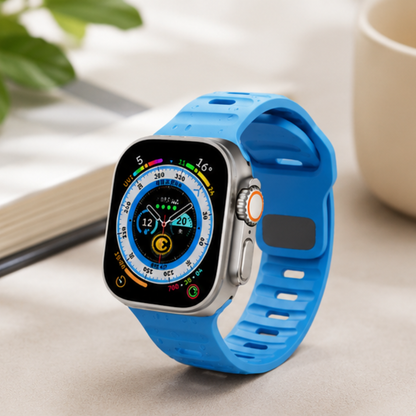 Apple Watch Ultra with a sky blue silicone sport band displayed on a light surface, showing the compass watch face in a lifestyle setting