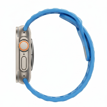 Side profile view of an Apple Watch Ultra with titanium case and bright blue silicone sport band on a white background, showcasing the band's sporty buckle design