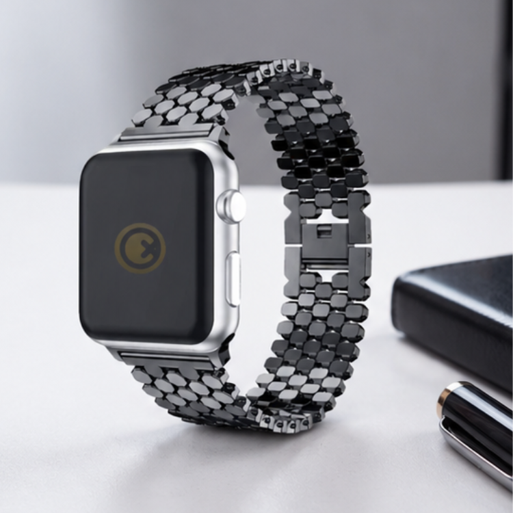 Apple Watch with silver stainless steel jubilee link band standing upright on a desk beside a laptop, showing the watch face and band detail
