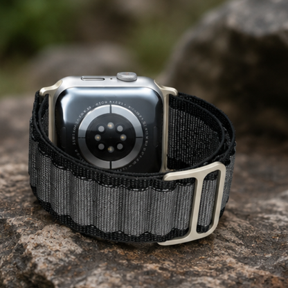 Apple Watch Ultra with charcoal grey woven alpine loop band standing upright on a rock outdoors, showing the silver G-hook buckle detail