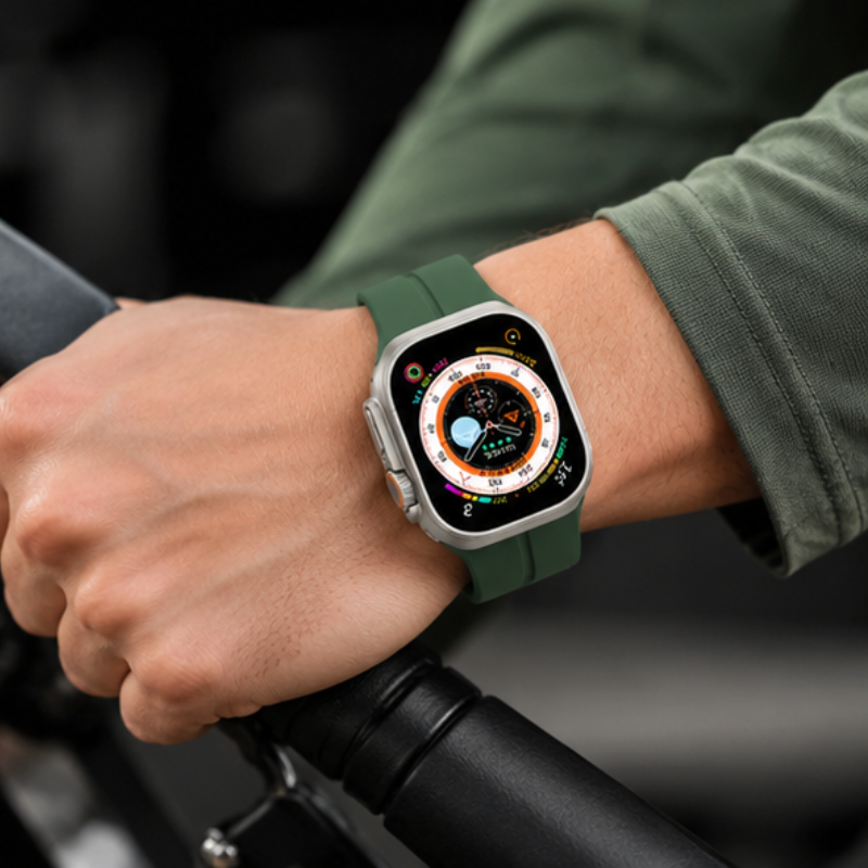Person in an olive green jacket wearing Apple Watch Ultra with forest green silicone sport band while gripping bicycle handlebars