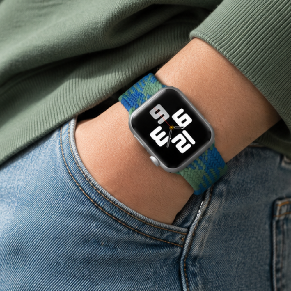 Close-up of a person in jeans and a green top wearing Apple Watch with blue and green braided solo loop band on their wrist