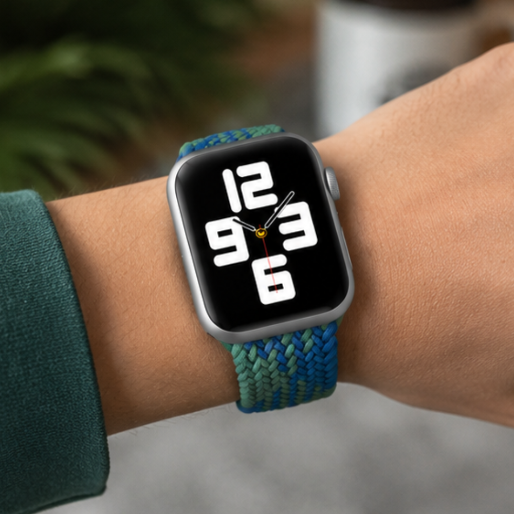 Person in a dark green top wearing Apple Watch with blue and green braided solo loop band, displaying a bold digital watch face