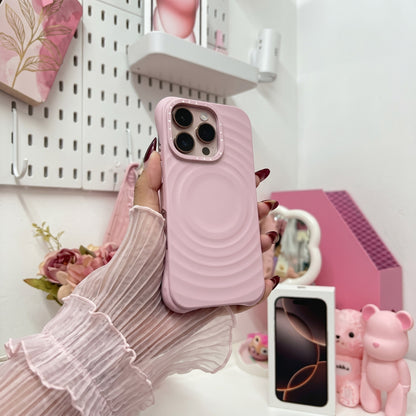 Pink wavy textured iPhone case with metal camera ring held in hand in aesthetic bedroom setting, surrounded by white pegboard organizer, pink flowers, and cute desk accessories