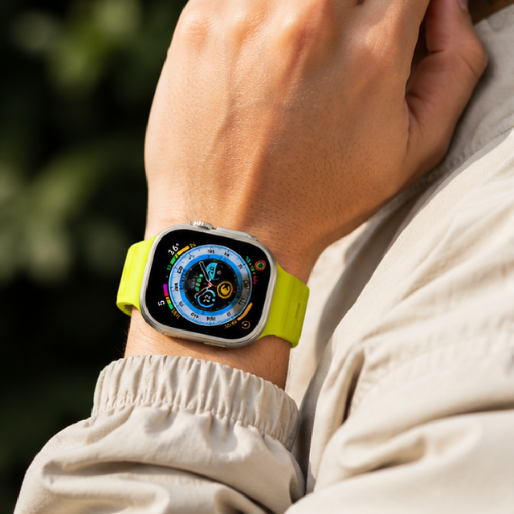 Person in a beige casual outfit wearing Apple Watch Ultra with neon yellow silicone sport band on their wrist outdoors