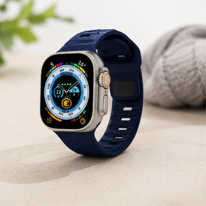 Apple Watch Ultra with a deep navy blue silicone sport band displayed on a neutral surface with a cozy knit fabric in the background