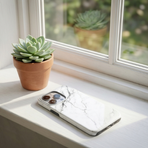 White marble-patterned iPhone case resting on a windowsill with a small succulent plant in the background | GrunX
