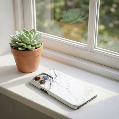 White marble-patterned iPhone case resting on a windowsill with a small succulent plant in the background | GrunX