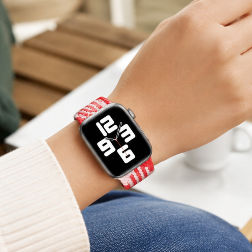 Person wearing an Apple Watch with a red and white braided solo loop band on their wrist, shown against a casual denim background