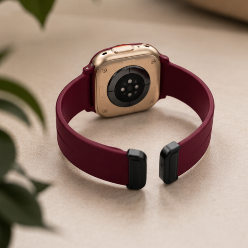 Rear view of Apple Watch Ultra with burgundy magnetic silicone loop band on a light surface, showing back sensors and magnetic clasp detail