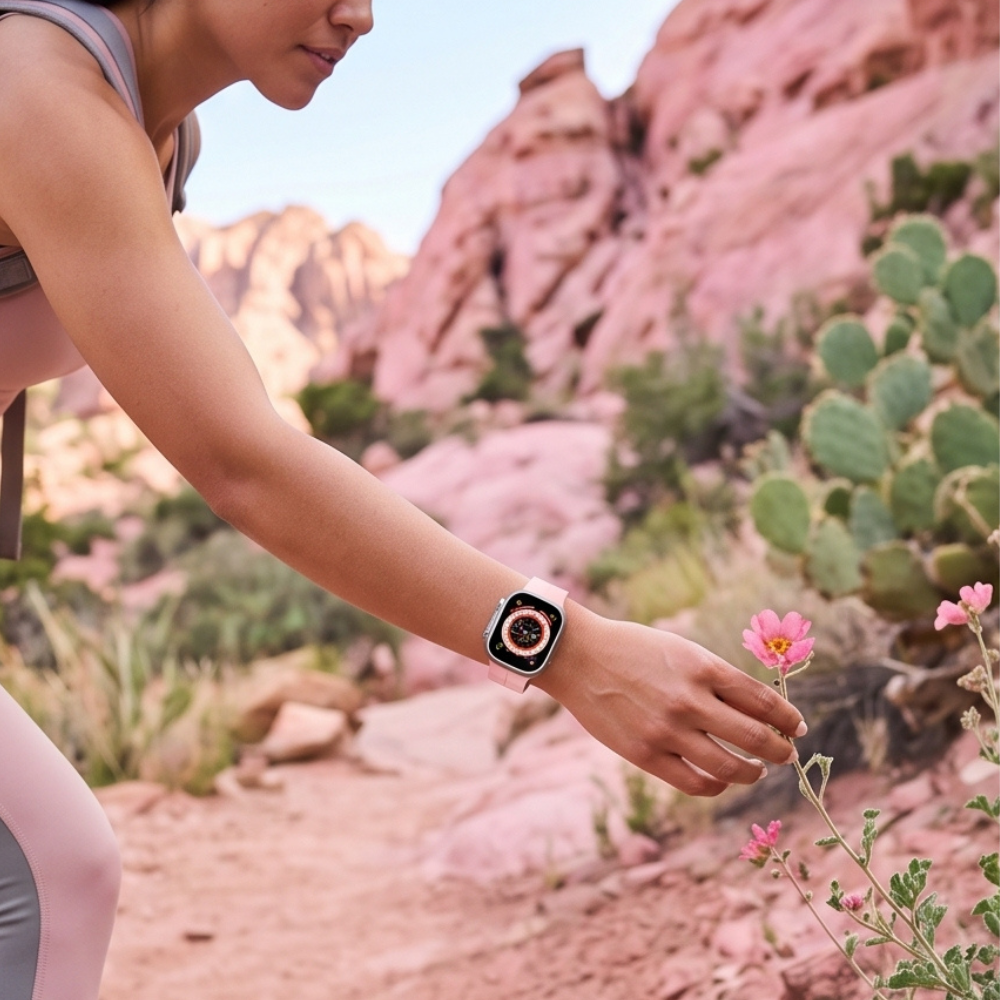 Pink edition smartwatch worn during outdoor fitness activity near pink desert flowers and cactus plants, showing active lifestyle capability