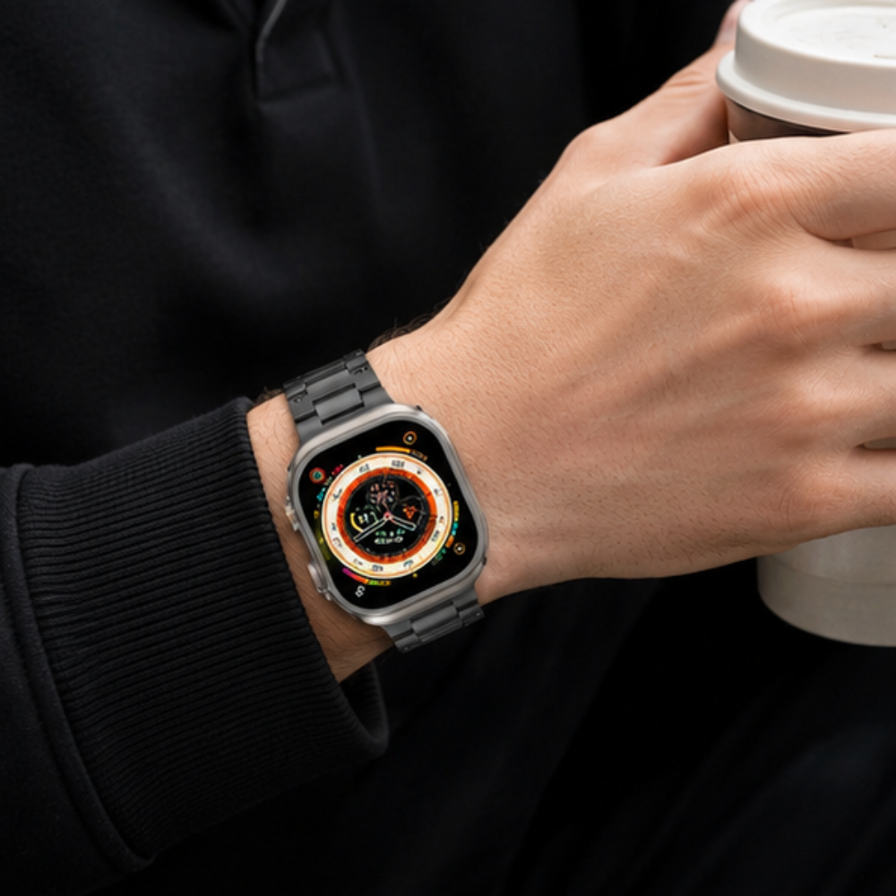 Person wearing Apple Watch Ultra with black metal link band on wrist, holding a coffee cup, dressed in a black sweatshirt