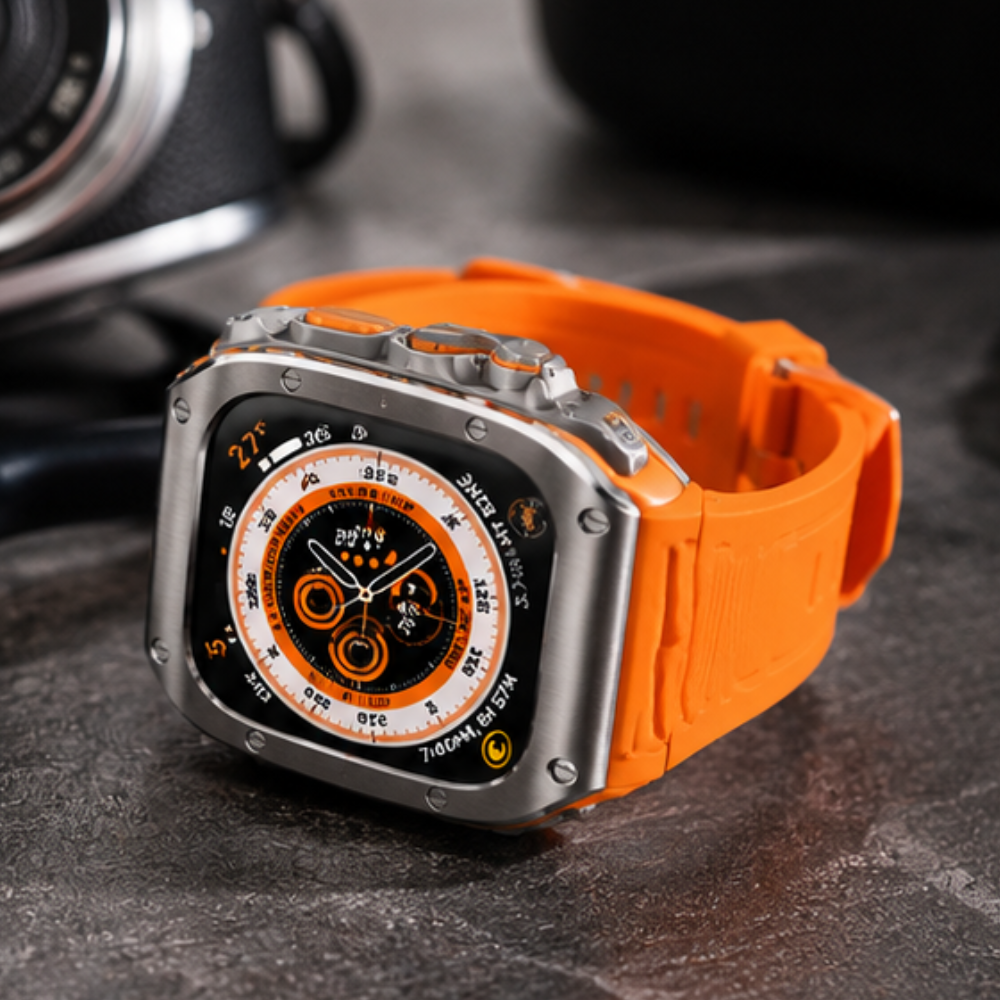 Angled close-up of Apple Watch Ultra with titanium case mod kit and orange rubber sport band displaying an orange compass watch face on a dark surface