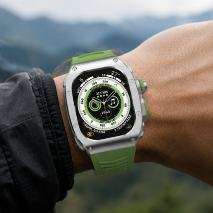 Person wearing Apple Watch Ultra with olive green rubber band on wrist against a blurred mountain landscape background
