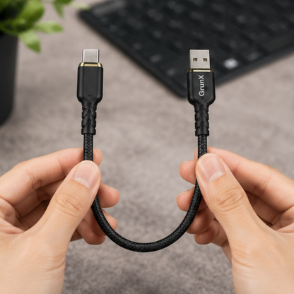Hands holding a short black USB Type-C to Type-A cable in front of a keyboard