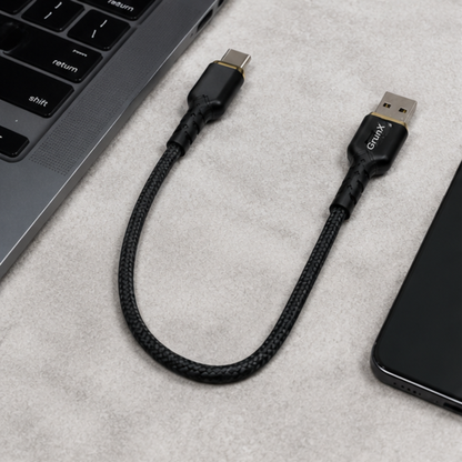 Short black USB Type-C to Type-A cable laid flat next to a laptop on a dark surface