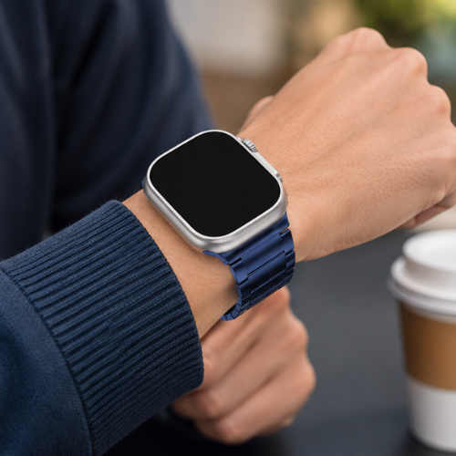 Person wearing Apple Watch Ultra with blue metal link band on wrist, dressed in a navy blue knit sweater, with a coffee cup in the background